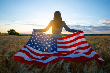 Wall Mural - Girl with the flag of America at the wheat field against the sunset