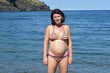  front view of pregnant woman standing on the beach looking at camera