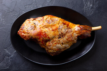 Wall Mural - Roasted lamb leg on a plate. Black background. Close up. Top view.