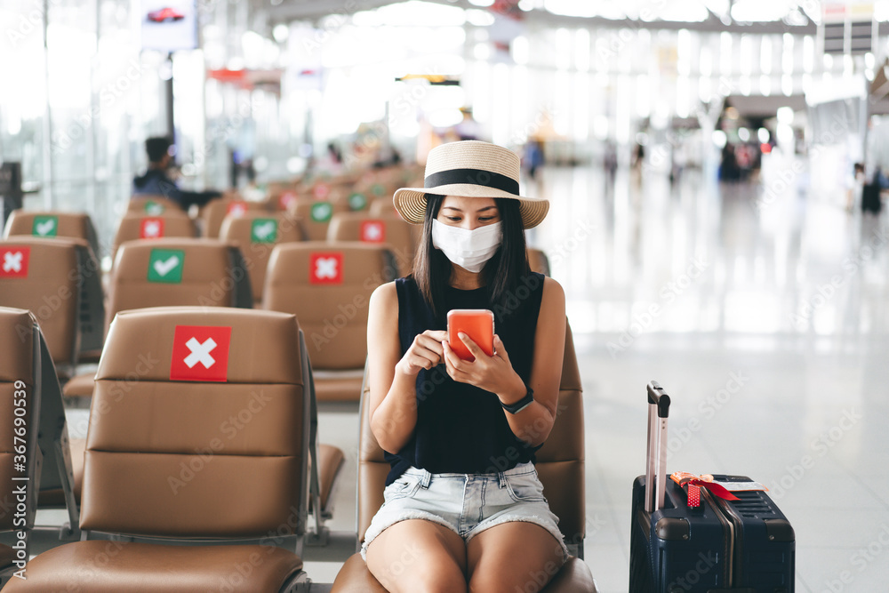 Young adult tourist woman wear mask for virus outbreak at airport terminal with social distancing chair. - obrazy, fototapety, plakaty 