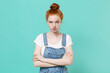 Perplexed displeased young readhead girl in casual denim clothes posing isolated on blue turquoise wall background studio portrait. People lifestyle concept. Mock up copy space. Holding hands crossed.