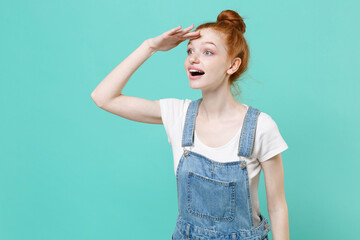 Wall Mural - Amazed young readhead girl in casual denim clothes posing isolated on blue turquoise background studio. People lifestyle concept. Mock up copy space. Hold hand at forehead looking far away distance.