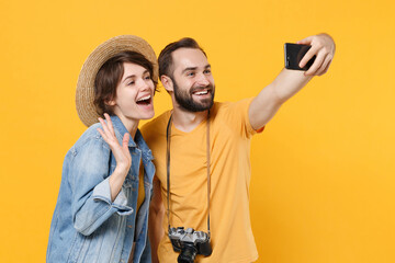 Wall Mural - Cheerful tourists couple friends guy girl in summer clothes, hat isolated on yellow background. Passenger traveling abroad on weekends. Air flight journey concept. Doing selfie shot on mobile phone.