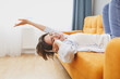 © ViDi Studio - Joyful funny young woman girl in casual clothes lying on couch spending time in living room at home. Rest relax good mood leisure lifestyle concept. Mock up copy space. Listen music with headphones.