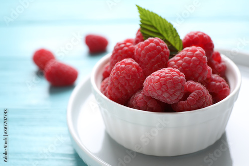 Cuadros en Lienzo Delicious ripe raspberries in bowl on light blue wooden table, closeup