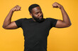 © ViDi Studio - Strong african american man guy football fan in casual black t-shirt isolated on yellow wall background studio portrait. People emotions lifestyle concept. Mock up copy space. Showing biceps, muscles.
