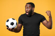 © ViDi Studio - Shocked african american man guy football fan in black t-shirt isolated on yellow background. Sport family leisure lifestyle concept. Cheer up support favorite team with soccer ball, clenching fist.