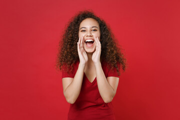 Wall Mural - Cheerful young african american woman girl in casual t-shirt posing isolated on red background studio portrait. People lifestyle concept. Mock up copy space. Screaming with hands gesture near mouth.
