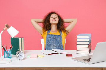 Relaxed african american girl employee in office sit work at desk isolated on pink background. Achievement business career. Education in school university college concept. Holding hands behind head.