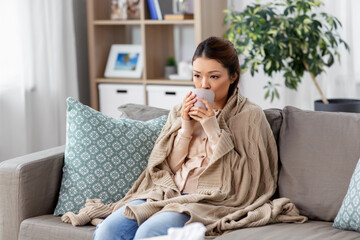 Wall Mural - health, cold and people concept - sad sick young asian woman in blanket drinking hot tea at home
