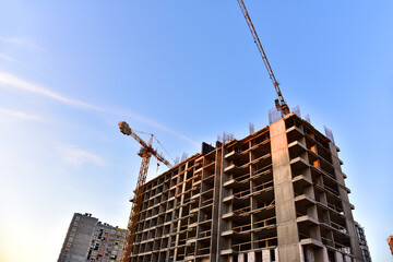 Tower cranes working at construction site on blue sky background. Construction process of the new modern residential buildings.Tall house renovation project, government programs.