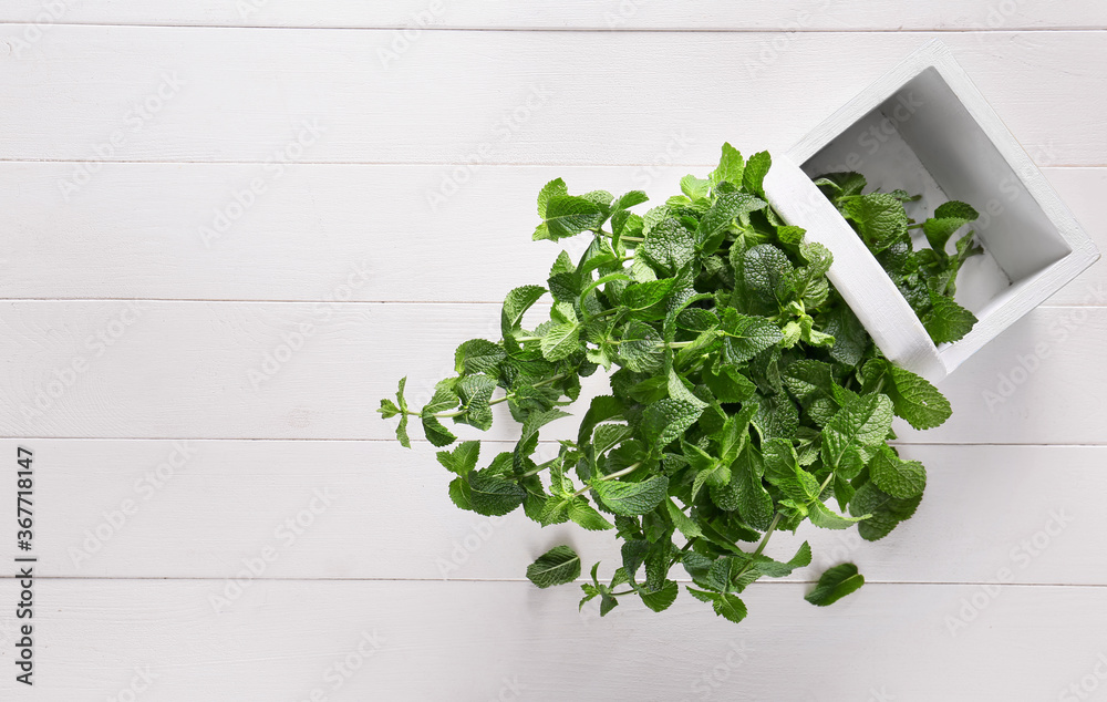 Fresh green mint in basket on white wooden background