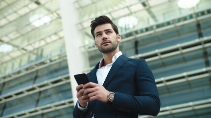 Portrait businessman using phone. Man looking away in stylish suit at street