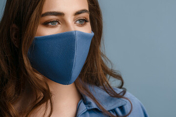 Woman wearing stylish protective blue face mask. Young beautiful brunette model. Trendy Fashion accessory during quarantine of coronavirus pandemic. Close up studio portrait. Copy, empty space