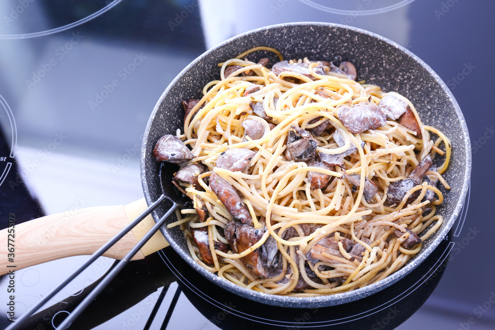 Frying pan with tasty pasta and mushrooms on stove