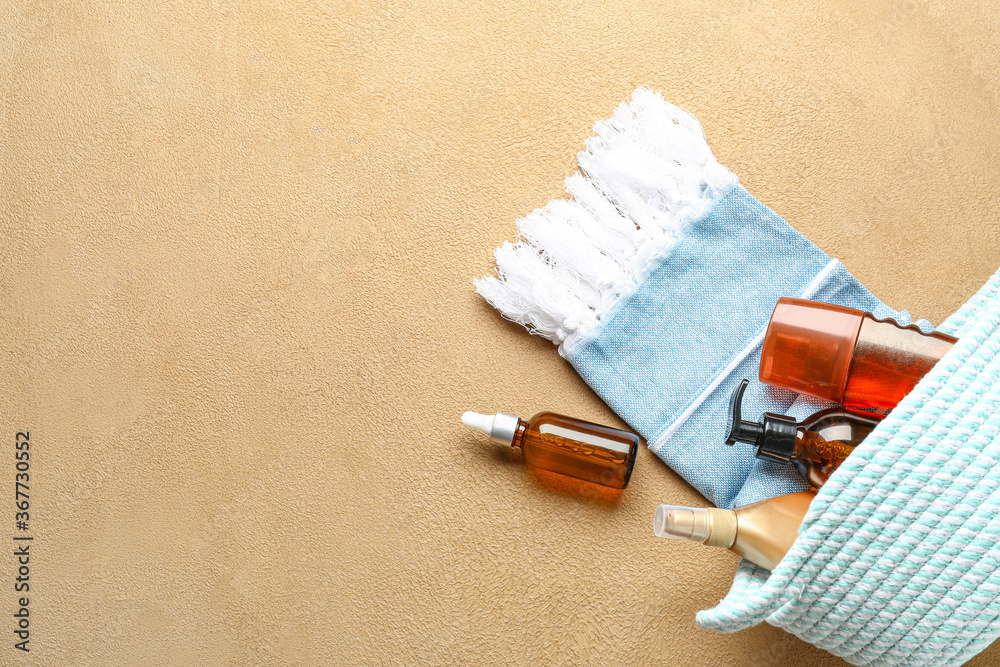 Bag with sunscreen cream and towel on color background
