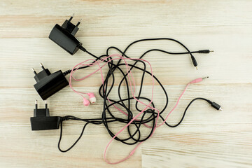 the need for universal battery charger: black 3 different chargers with different connectors and earphones tangled cables together, on the white oak table