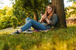 © Drobot Dean - Young blonde woman using smartphone under tree in park
