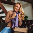 Happy adult woman opening cardboard box with order sitting on sofa in living room, online shopping delivery concept