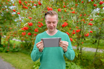 Portrait of young handsome blond man with digital tablet outdoors