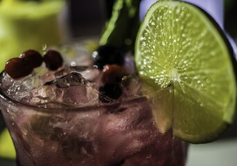 Poster - Closeup of a delicious cocktail with ice and berries and a slice of lime under the lights