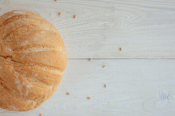 Wall Mural - A loaf of wheat bread on a white wooden background with wheat grains. Copy space. Top view.