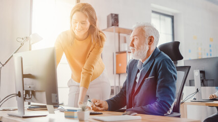 Poster - Handsome Middle Aged Creative Engineer Sitting at the Desk working on Desktop Computer Has Discussion with Beautiful Female Project Manager. Shot in Modern Office with Warm Sun Flare