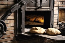 Closeup Shot Of Two Loaves Of Freshly Baked Bread Being Taken Out Of An Old Masonry Brick Oven