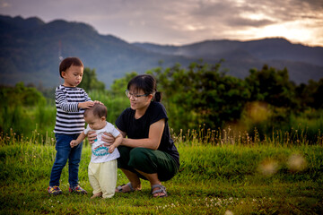 On evening time, The Oriental mother happily with two sons, One is kid and one is boy infant.