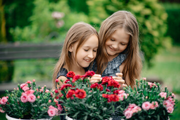 Two little beautiful girls in dresses are looking after the blossoming flowers. Nature outside the city and fresh air. Healthy lifestyle concept. Carefree childhood.