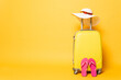 yellow travel bag with flip flops, sun hat and sunglasses isolated on yellow