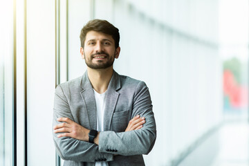 Wall Mural - Confident businessman standing with arms folded at modern office