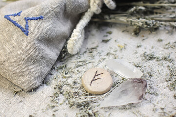 Wall Mural - Scandinavian wooden rune Fehu, Fe, Feoh on a rough linen cloth with amethyst crystalline, rock crystal and dried wormwood