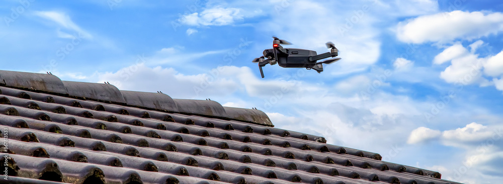 Drone in the air inspecting the roof over the house. Close-up of drone and roof. - obrazy, fototapety, plakaty 