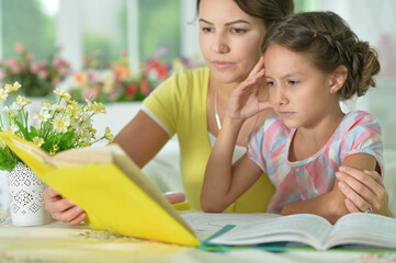 Poster - Cute girl reading book with mother at the table at home