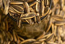 Fried Sunflower Seeds In A Glass Cup And Sunflower Seeds Scattered. Close Up.