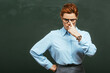 © LIGHTFIELD STUDIOS - serious teacher touching eyeglasses while standing with hand on hip near chalkboard