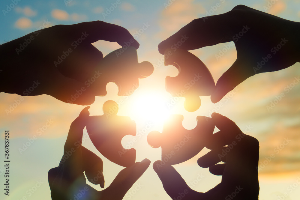 Four hands of businessmen put together a puzzle against the backdrop of a dramatic sky at sunset. Business concept idea, collaboration, teamwork, partnership, innovation - obrazy, fototapety, plakaty 