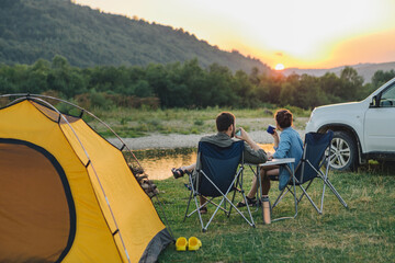 couple sitting in camp chairs looking at sunset above river in mountains