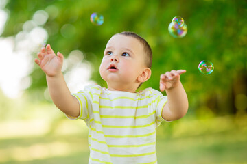 Wall Mural - Happy baby boy one year plays with soap bubbles summer outdoors. Children's Lystyle