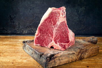 Raw dry aged wagyu porterhouse beef block offered as close-up on black rustic wooden board with copy space