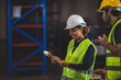 © chokniti - Group of warehouse workers logistic team  wearing hardhats working in aisle between tall racks with packed goods