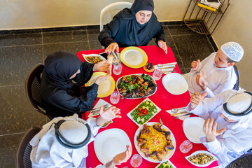 Wall Mural - Happy Arabic Muslim family praying to god prior eating and asking for forgiveness