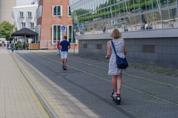 Wall Mural - People ride E-scooters, trendy urban transportation with Eco friendly sharing  mobility concept, on bicycle lane at promenade riverside of Rhine River at medienhafen in Düsseldorf, Germany.