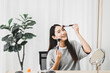 © gballgiggs - Beautiful asian woman applying and makeup on her face with brush,Beauty concept