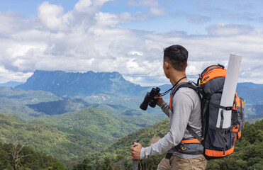 Travel male with backpack and holding a binoculars looking on top of mountain