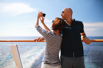 bald man and brunette woman traveling on cruise liner ship and taking pictures from smartphone on balcony 