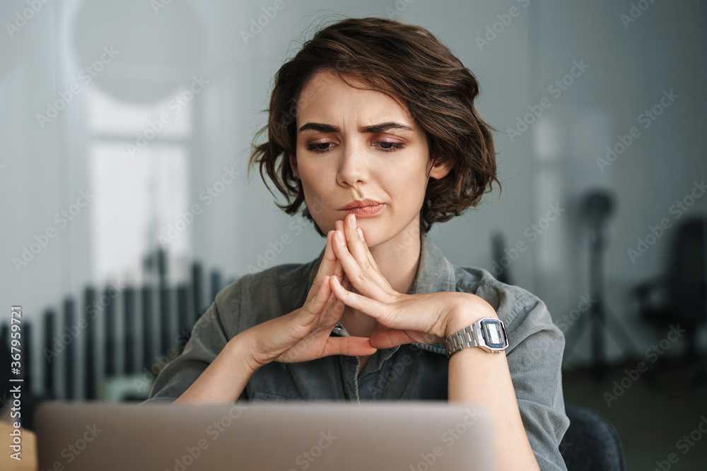 Image of young brooding woman working with laptop while sitting at ...