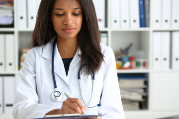 Wall Mural - Beautiful smiling black female doctor hold clipboard pad and fill something with silver pen. Physical illness prevention prescribe remedy ward round therapeutist assistance healthy lifestyle concept