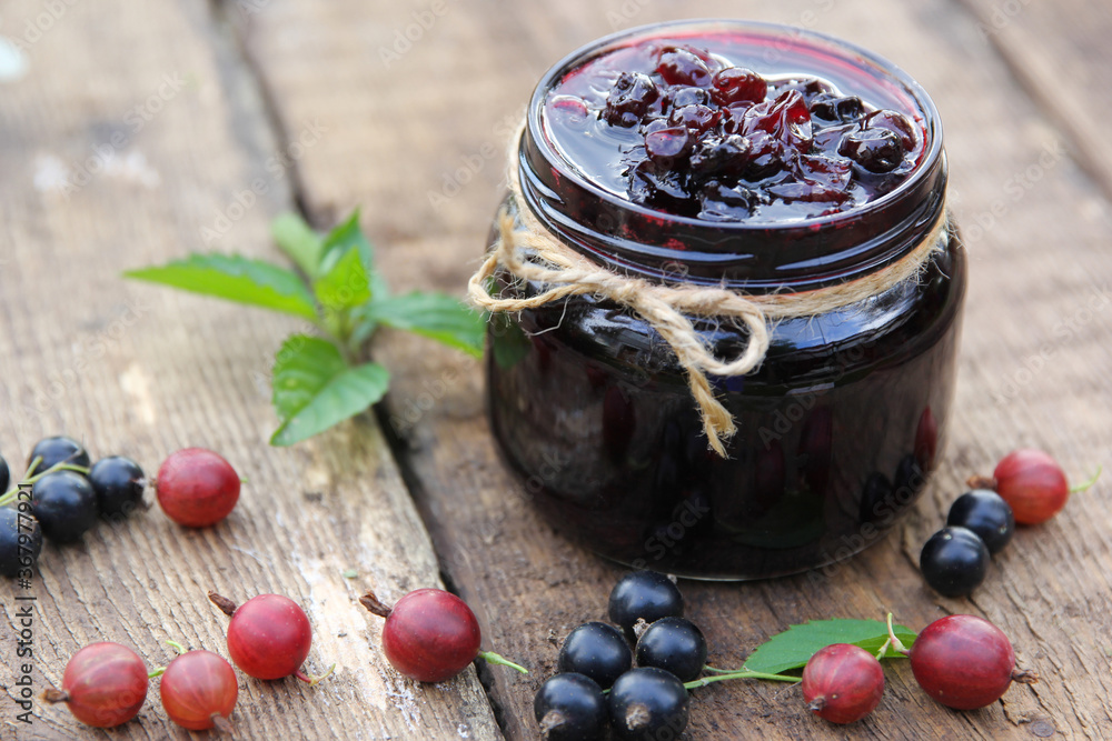 Berry jam in a jar. Preservations. Black currant and gooseberry jam, fresh mint and chamomile on an old wooden table. Rustic. Background image, copy space, horizontal - obrazy, fototapety, plakaty 